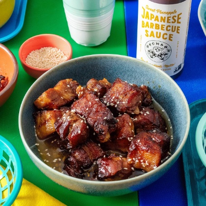 Bottle of Bachan‚ Sweet Pineapple Japanese BBQ Sauce surrounded by rice, sesame seeds and BBQ pork.