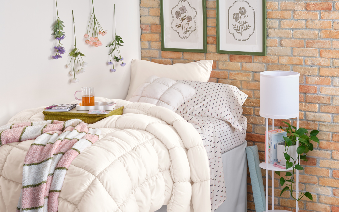 a dorm room decorated with a puffer comforter and art on the brick wall